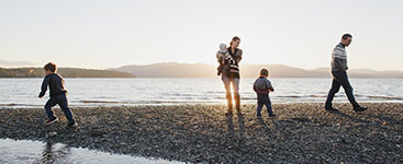 Édesanya gyermekét tartja miközben az apával és két másik gyermekükkel a vízparton sétálnak